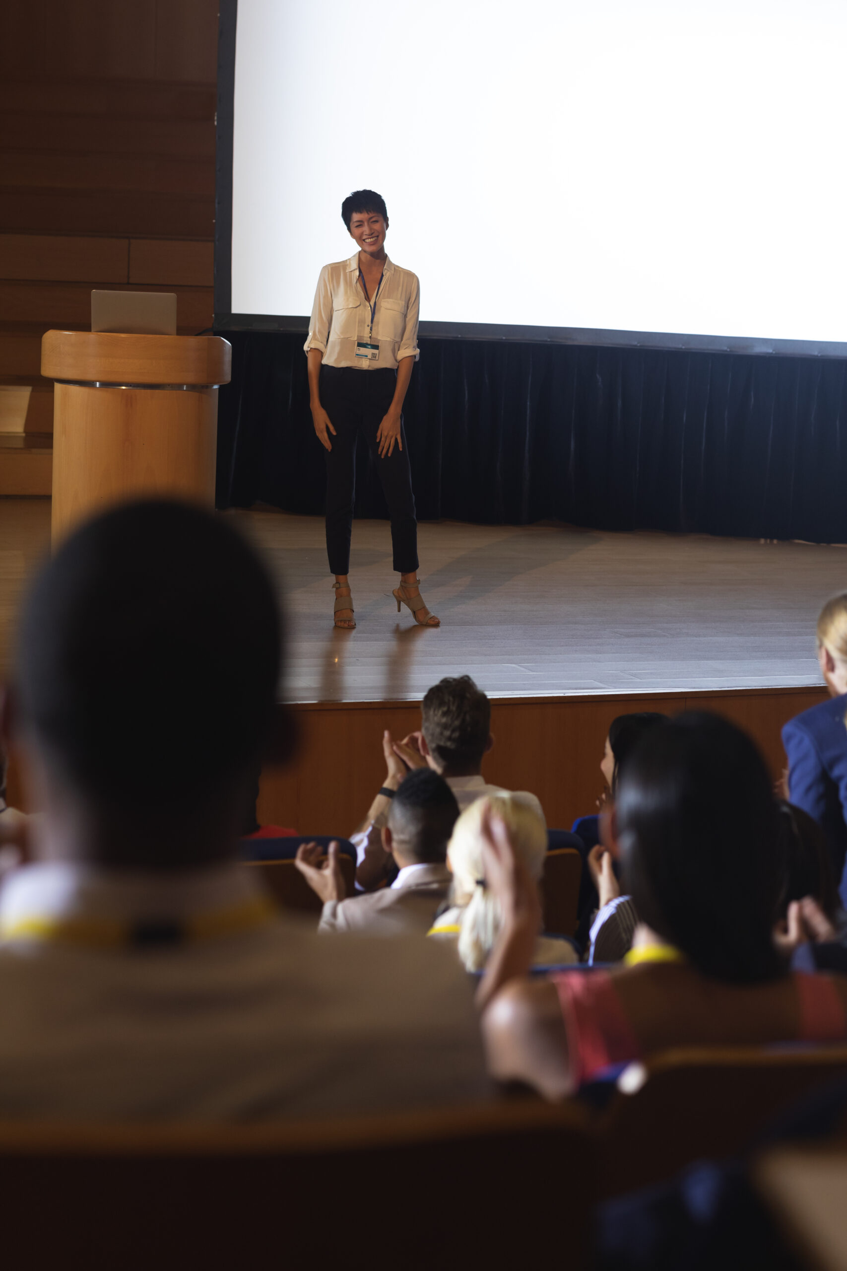Front view of beautiful Asian businesswoman standing and giving presentation in front of the audience in auditorium