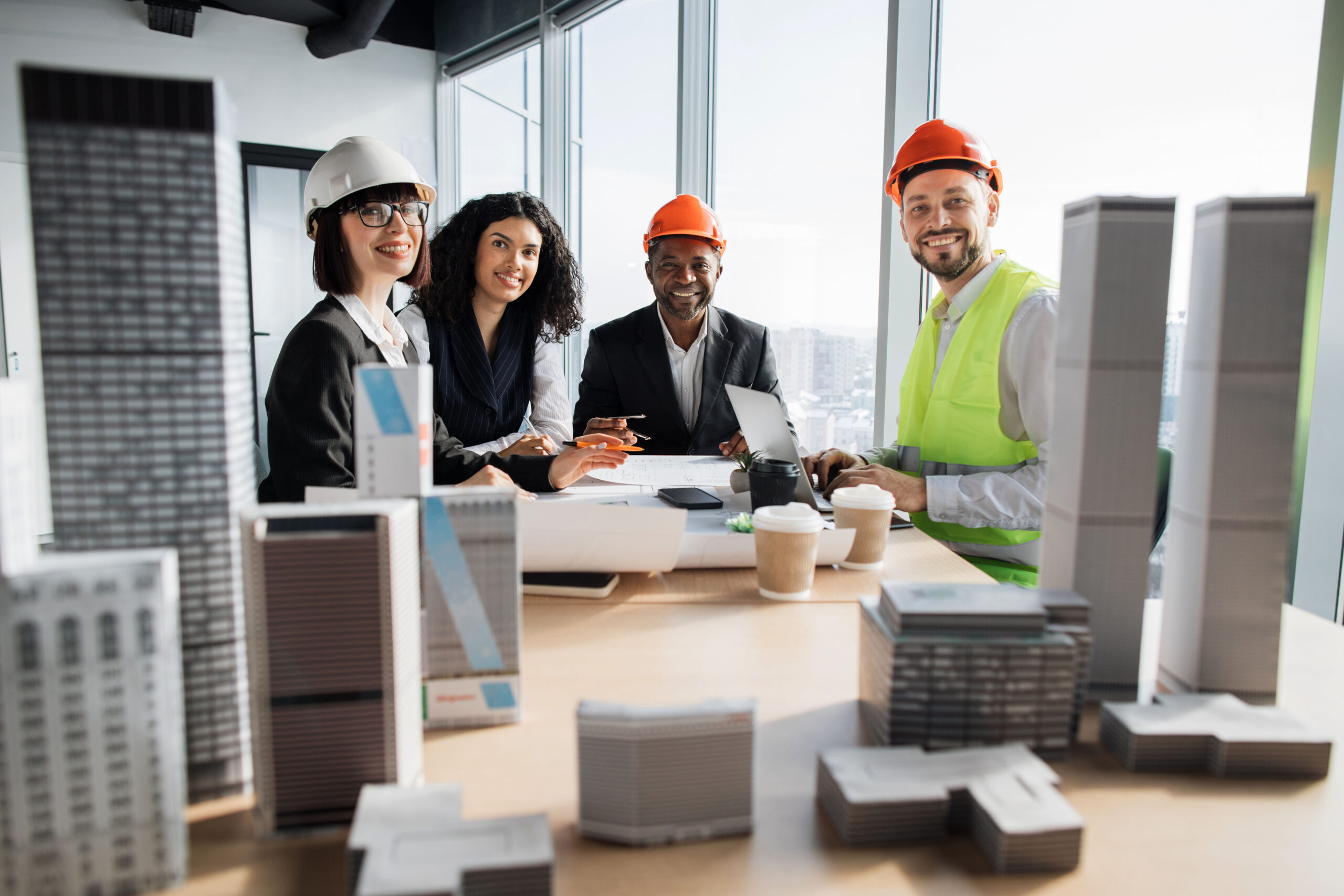 Multiracial coworkers builders and architects sitting at table with blueprints, gadgets and design of buildings residential project maquette and looking at camera.
